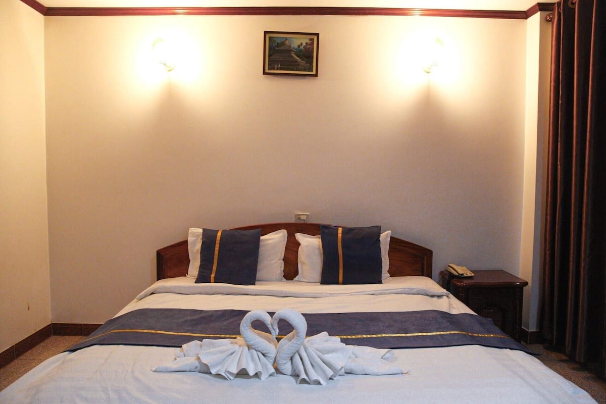 A hotel room with a neatly made bed, a bedside table with a phone, and a picture on the wall.