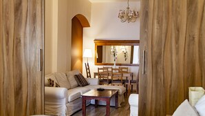 A hotel room with a wooden wardrobe, a sofa, a dining table with chairs, and a mirror. - Lounge Apartments (Kraków)