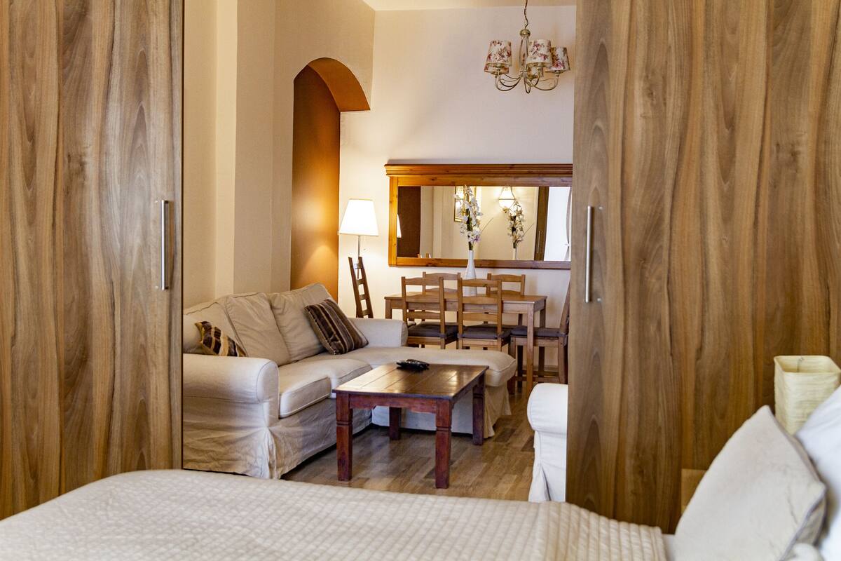 A hotel room with a wooden wardrobe, a sofa, a dining table with chairs, and a mirror.