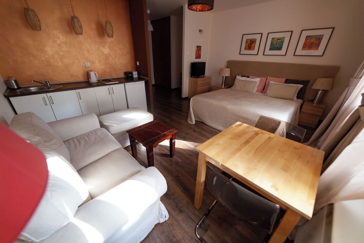 A hotel room with a sofa, a wooden table, a bed, a TV, and artwork on the wall.