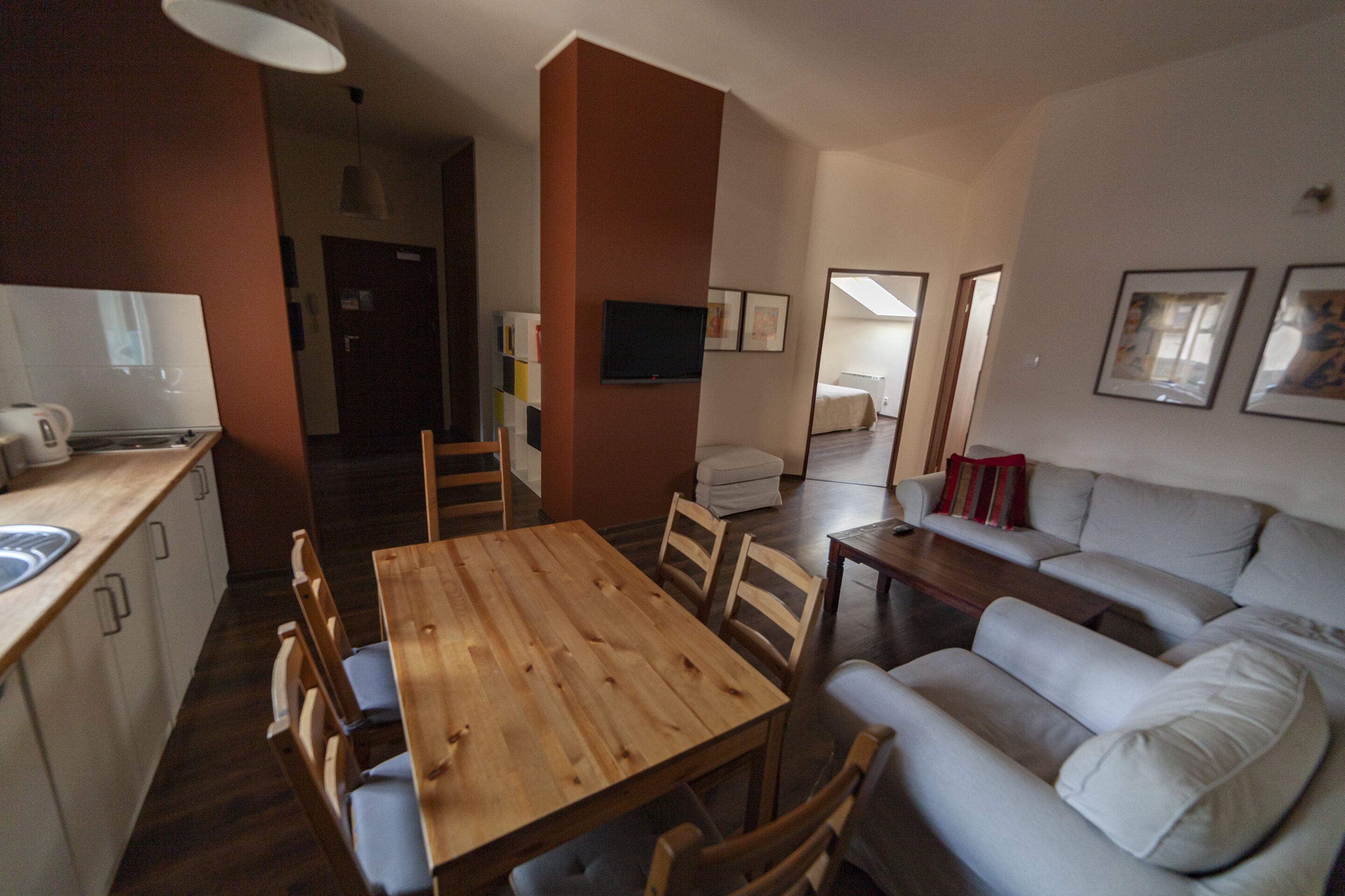 A modern living room with a wooden dining table, a sofa, and a TV mounted on the wall.