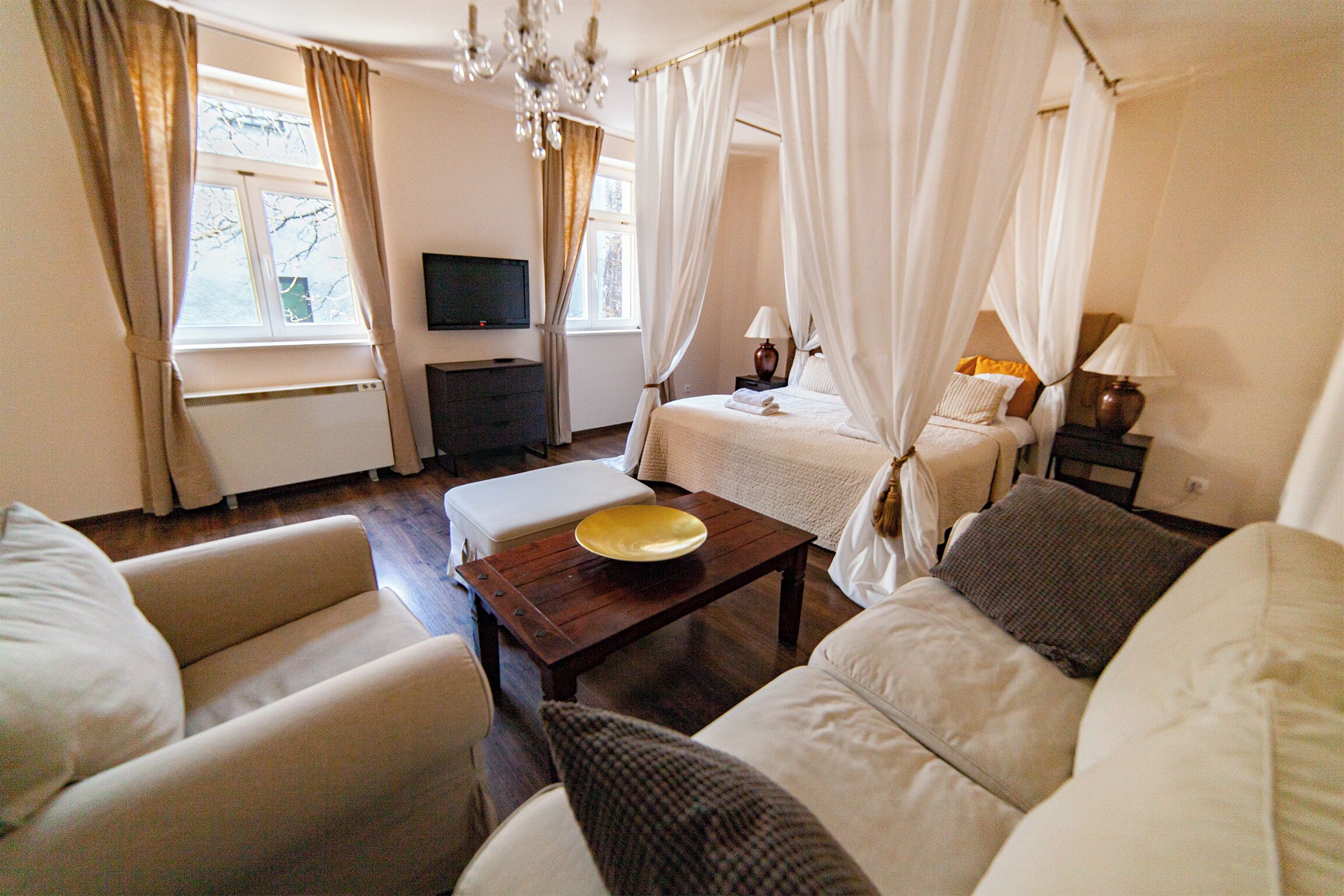 A bedroom with a bed, a bedside table, a TV, and a window with curtains.