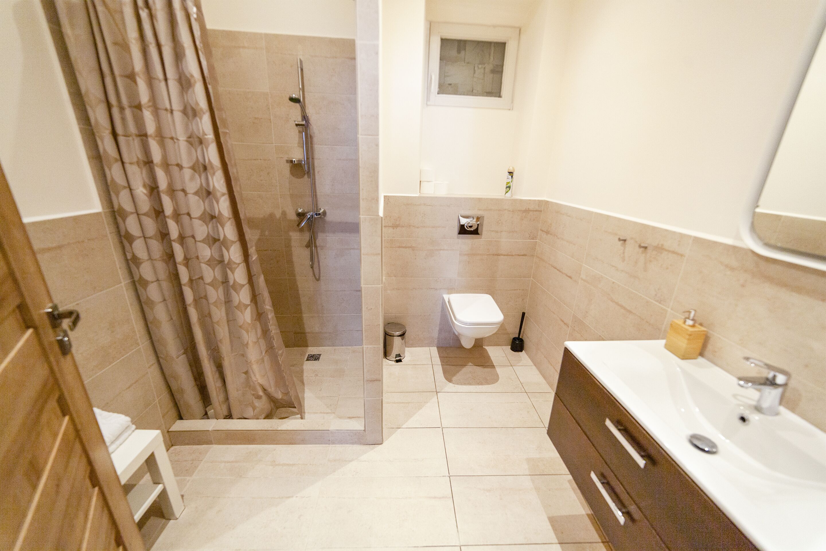 Baño con ducha, inodoro, lavabo y una ventana pequeña.