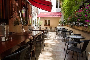 En udendørs patio med et træbord og stole, omgivet af krukker med planter og blomster.