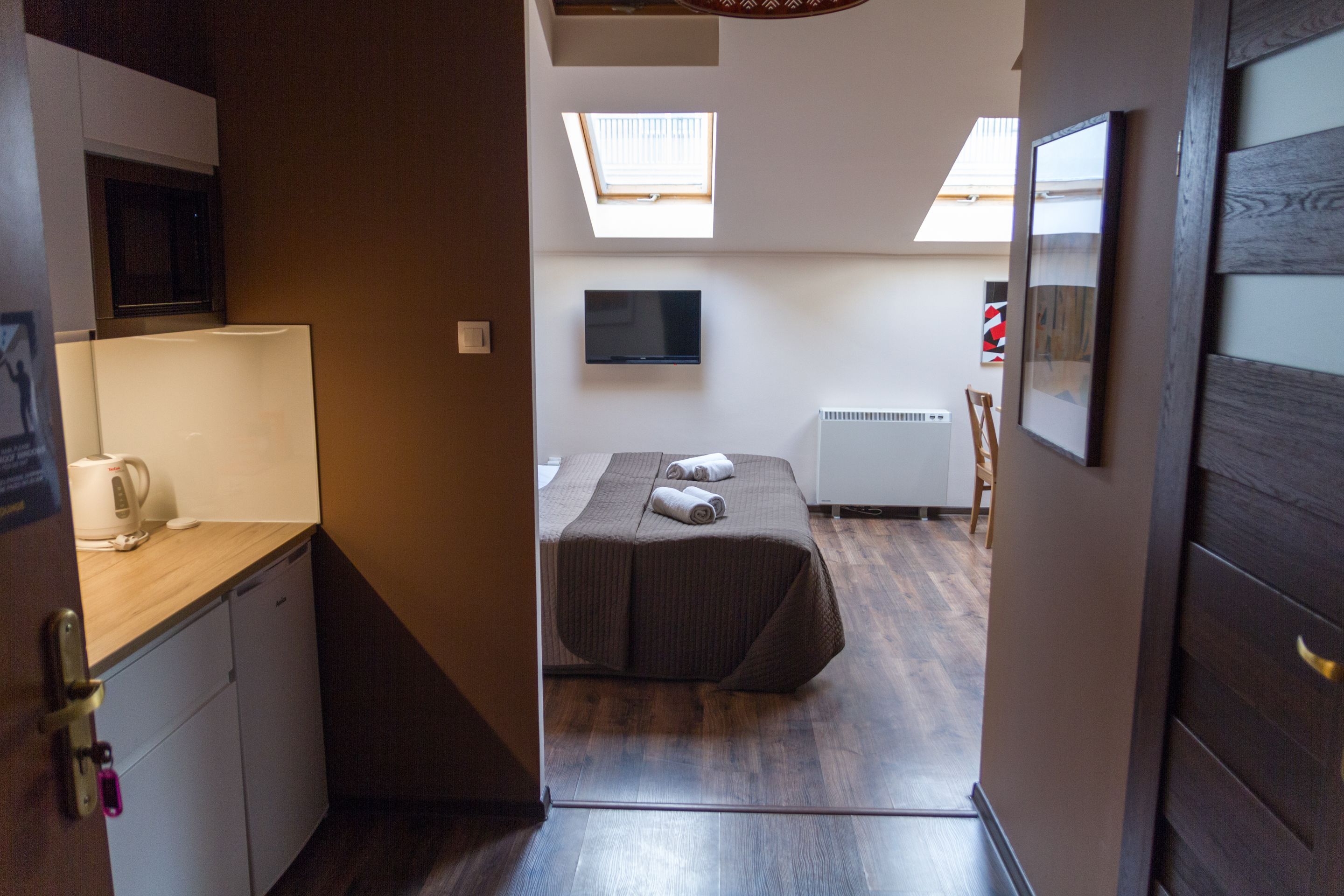 Une chambre d’hôtel de taille réduite, comprenant un lit, un bureau avec une lampe, une télévision et une petite kitchenette.