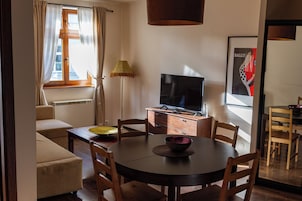 Spiseområde med et rundt bord, stole, et fjernsyn og en lampe.