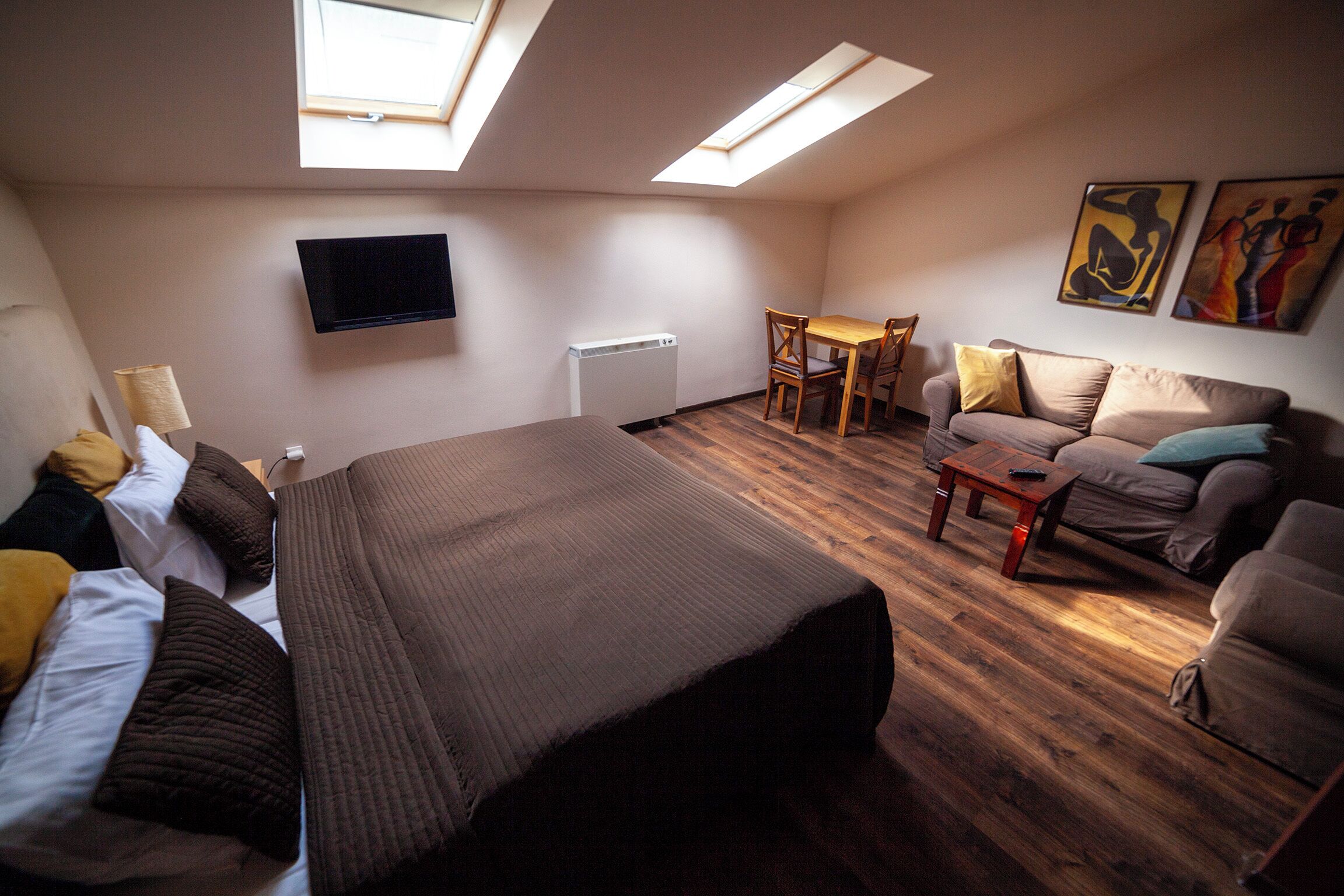 Ein Zimmer mit einem Bett, einem Sofa, einem Tisch und einem an der Wand befestigten Fernseher.