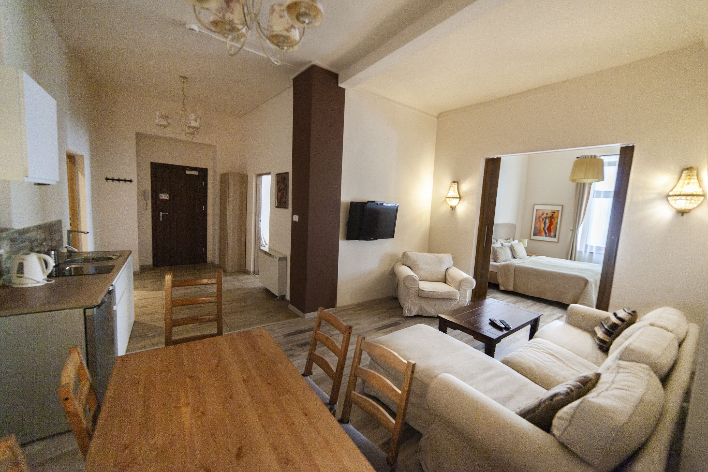 A spacious living area with a wooden dining table, a sofa set, and a kitchen area with a sink and stove.