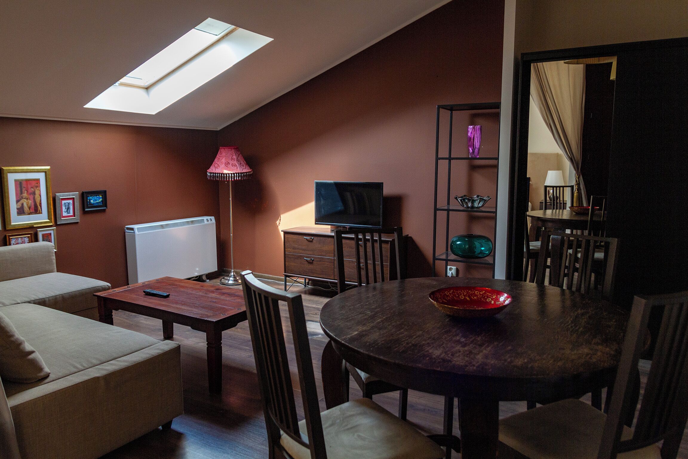 A living room with a sofa, a coffee table, a TV, a dining table with chairs, a lamp, and a bookshelf.