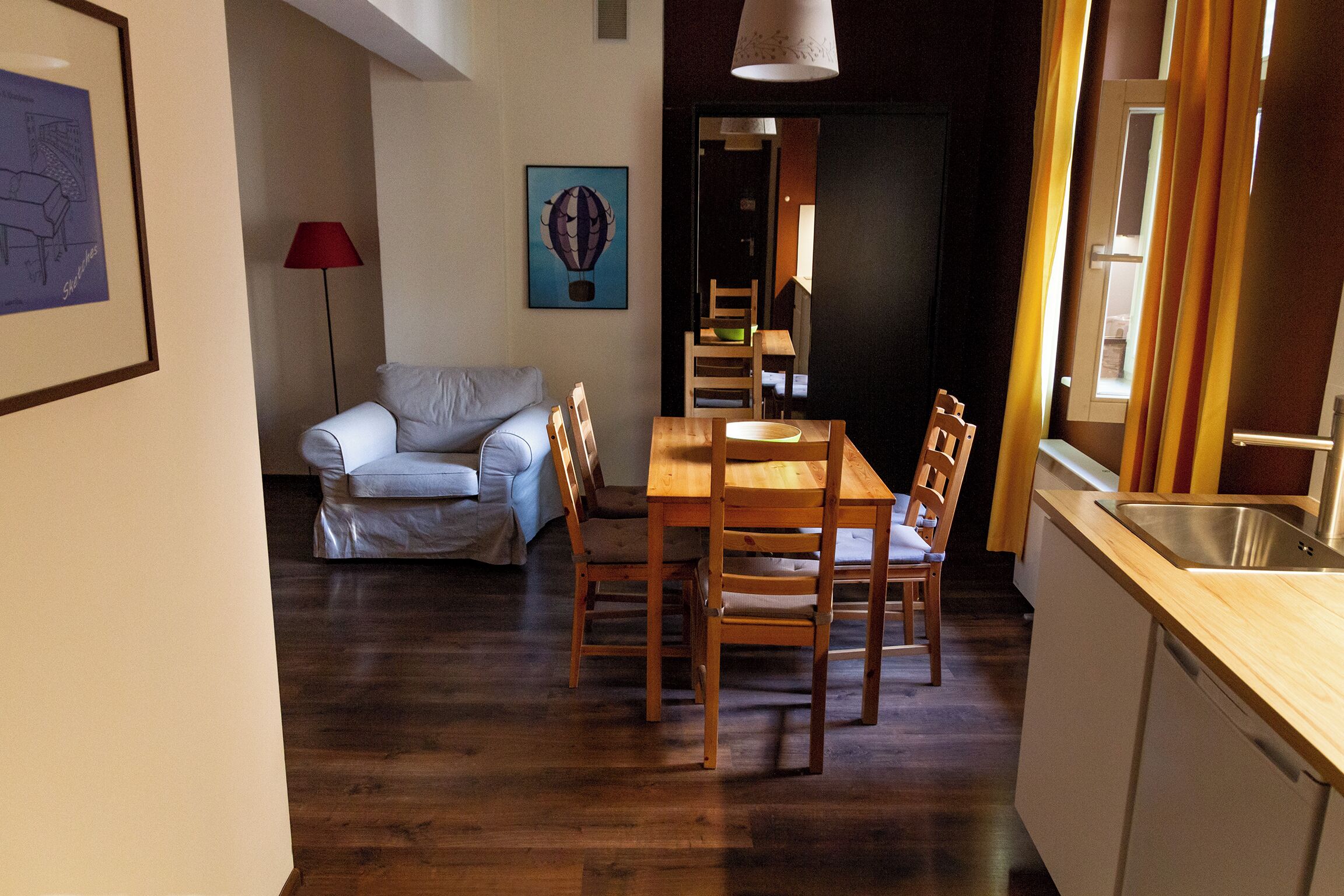 A dining area with a wooden table and chairs, a sofa, and a red floor lamp.