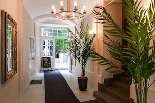 En gang med sort tæppe, en stor potteplante, en lysekrone og et skilt der viser, at lounge-kaffe er åben.