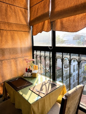 A dining area with a table set for two, a view of the city through a window, and a decorative item on the table. - Golden Moon Suite Hotel (Hanoi)
