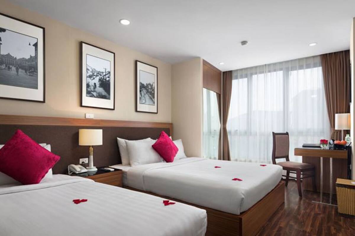 A hotel room with two beds, a desk, a chair, and a large window with curtains.