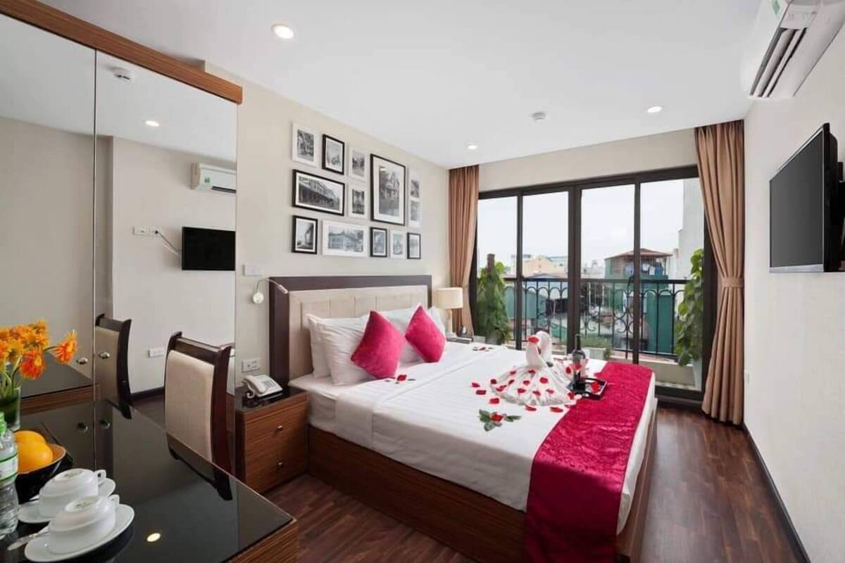A hotel room with a bed, bedside table, mirror, and a large window with a view.