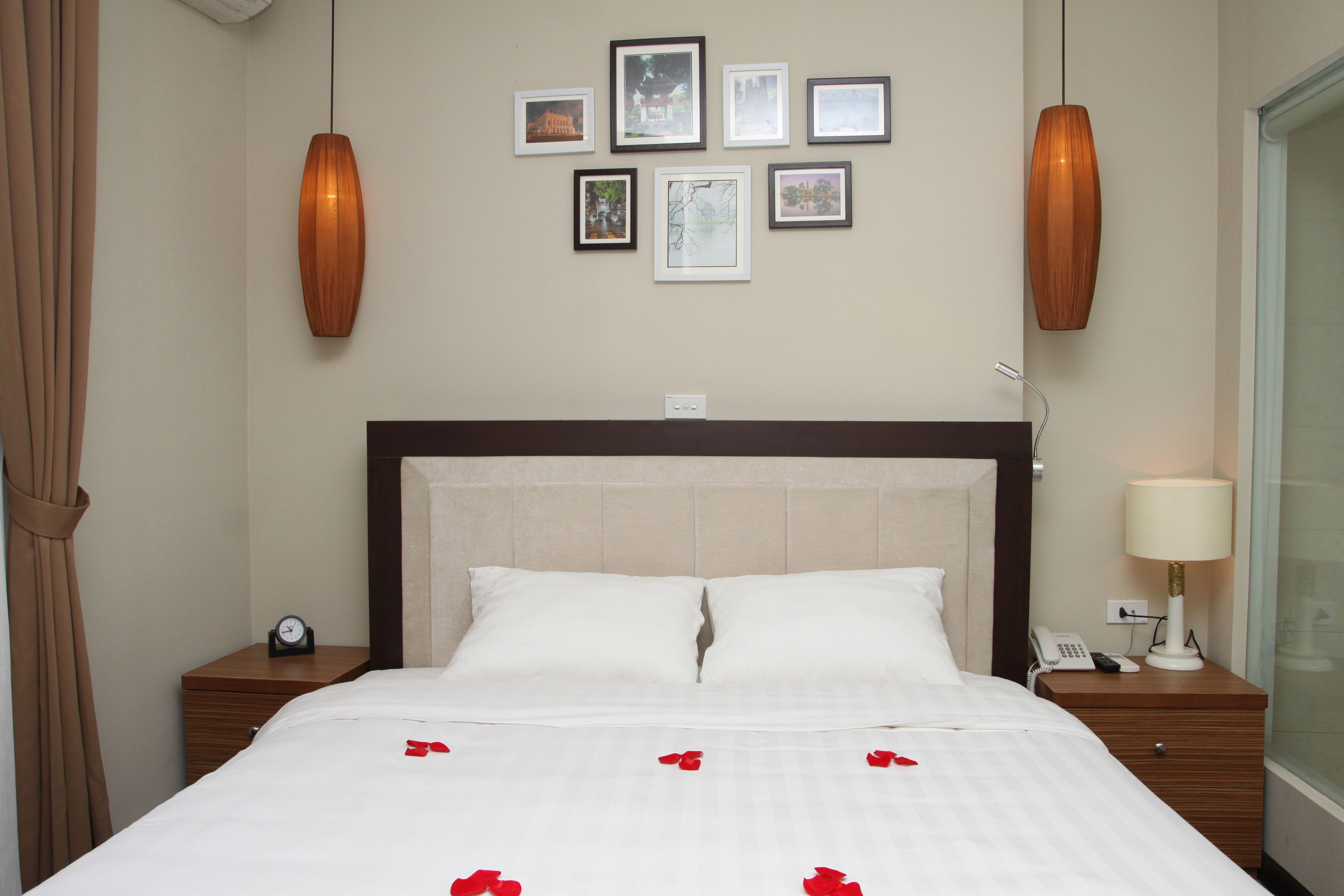 Habitación de hotel con una cama grande, dos mesitas de noche, un reloj en la pared, un teléfono y una lámpara.