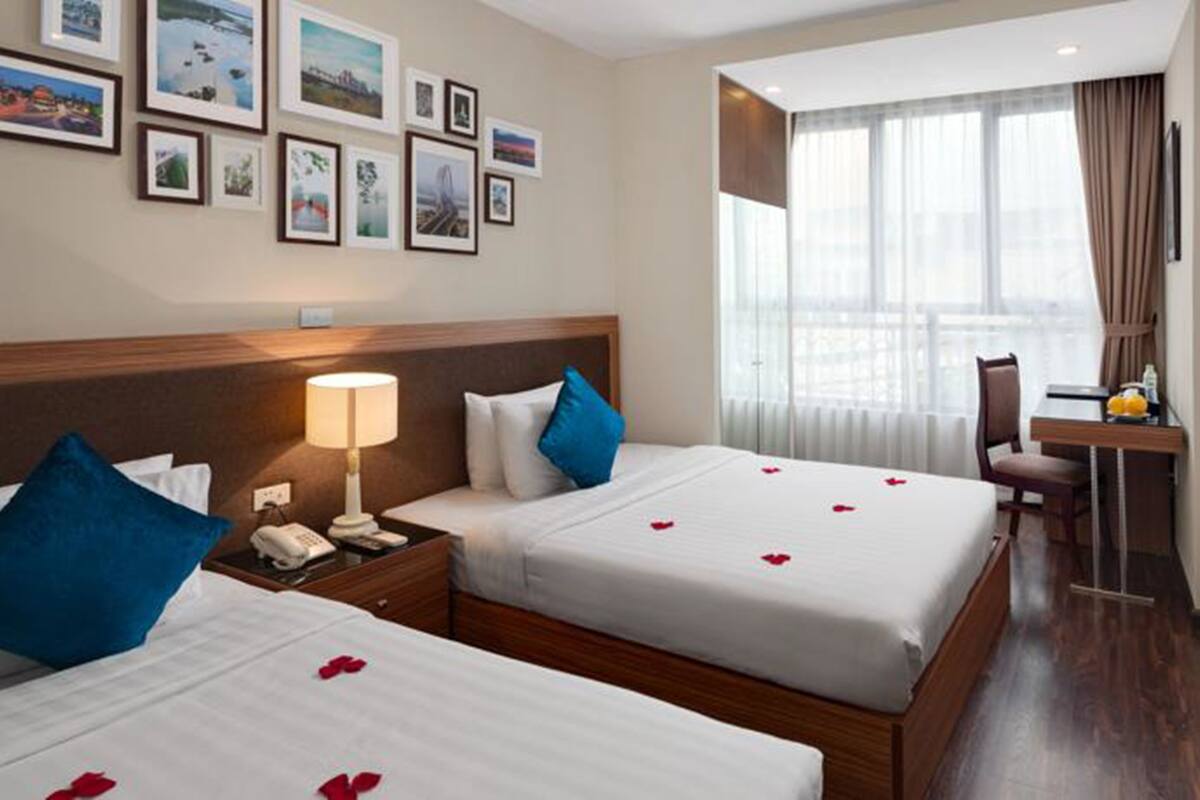 A hotel room with two beds, a desk, a TV, and a window with curtains.