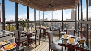 A restaurant with tables and chairs, a buffet with food, and a view of the city. - Golden Moon Suite Hotel (Hanoi)