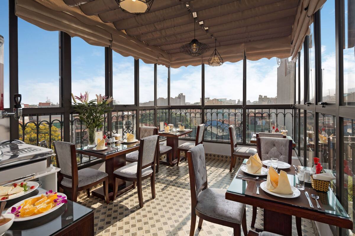 A restaurant with tables and chairs, a buffet with food, and a view of the city.