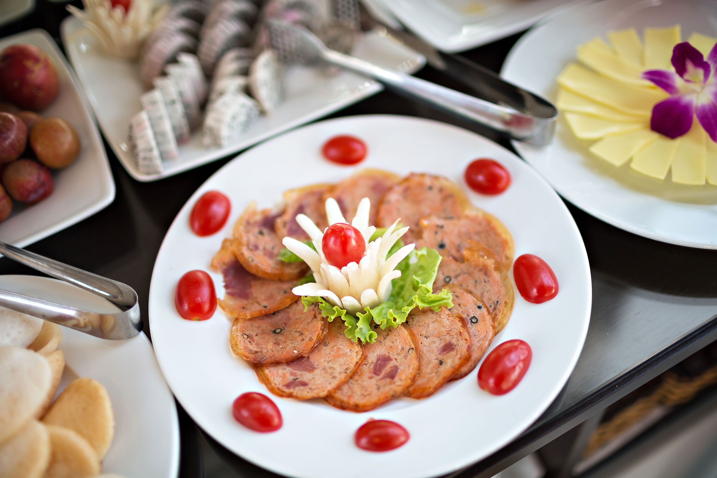 Variedad de alimentos en platos, incluyendo embutidos, tomates cherry y un arreglo floral decorativo.
