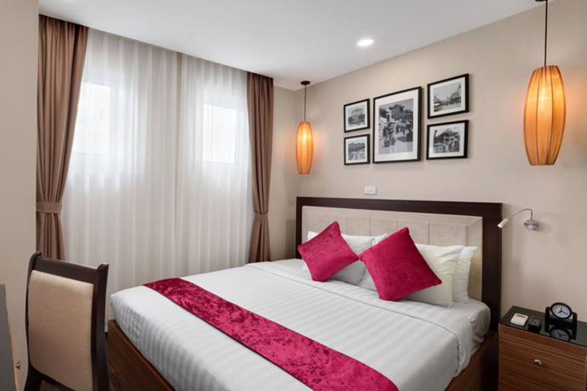 A hotel room with a large bed, a desk with a chair, a nightstand, and a window with curtains.