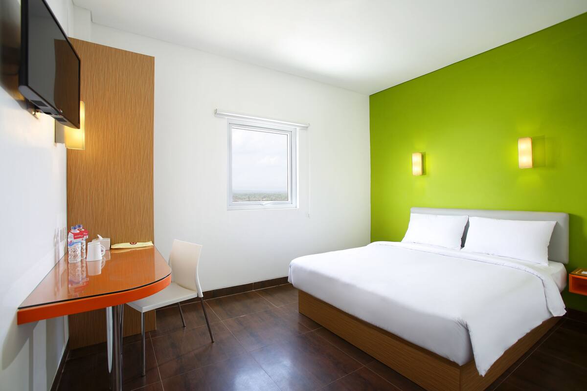 Une chambre d’hôtel avec un lit, une petite table, une chaise, un téléviseur et une fenêtre.
