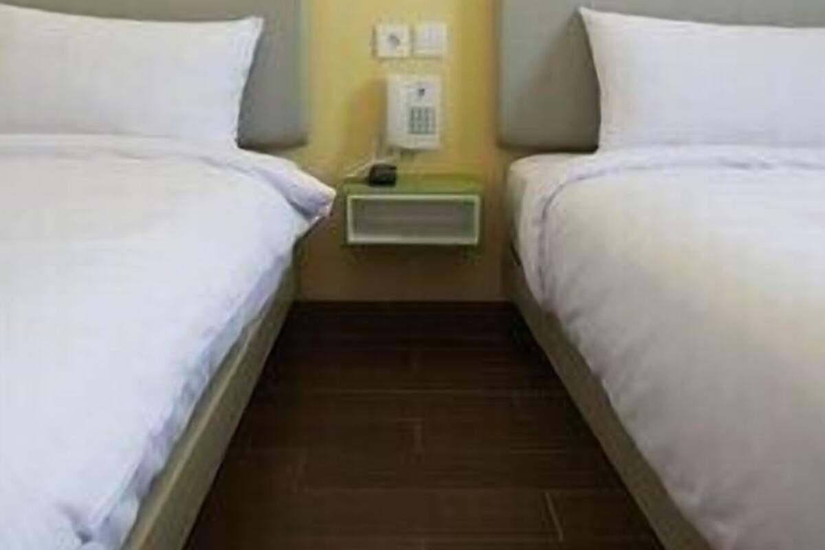 Une chambre d’hôtel avec deux lits simples, une table de chevet, un téléphone fixé au mur et un interrupteur.