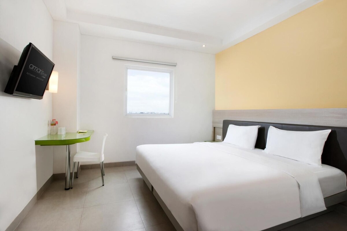 Une chambre d’hôtel avec un lit, un bureau, une chaise, une télévision et une fenêtre.