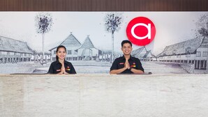 Two individuals seated at a reception desk with a backdrop of a traditional building illustration. - Amaris Hotel Pettarani Makassar (Makassar)