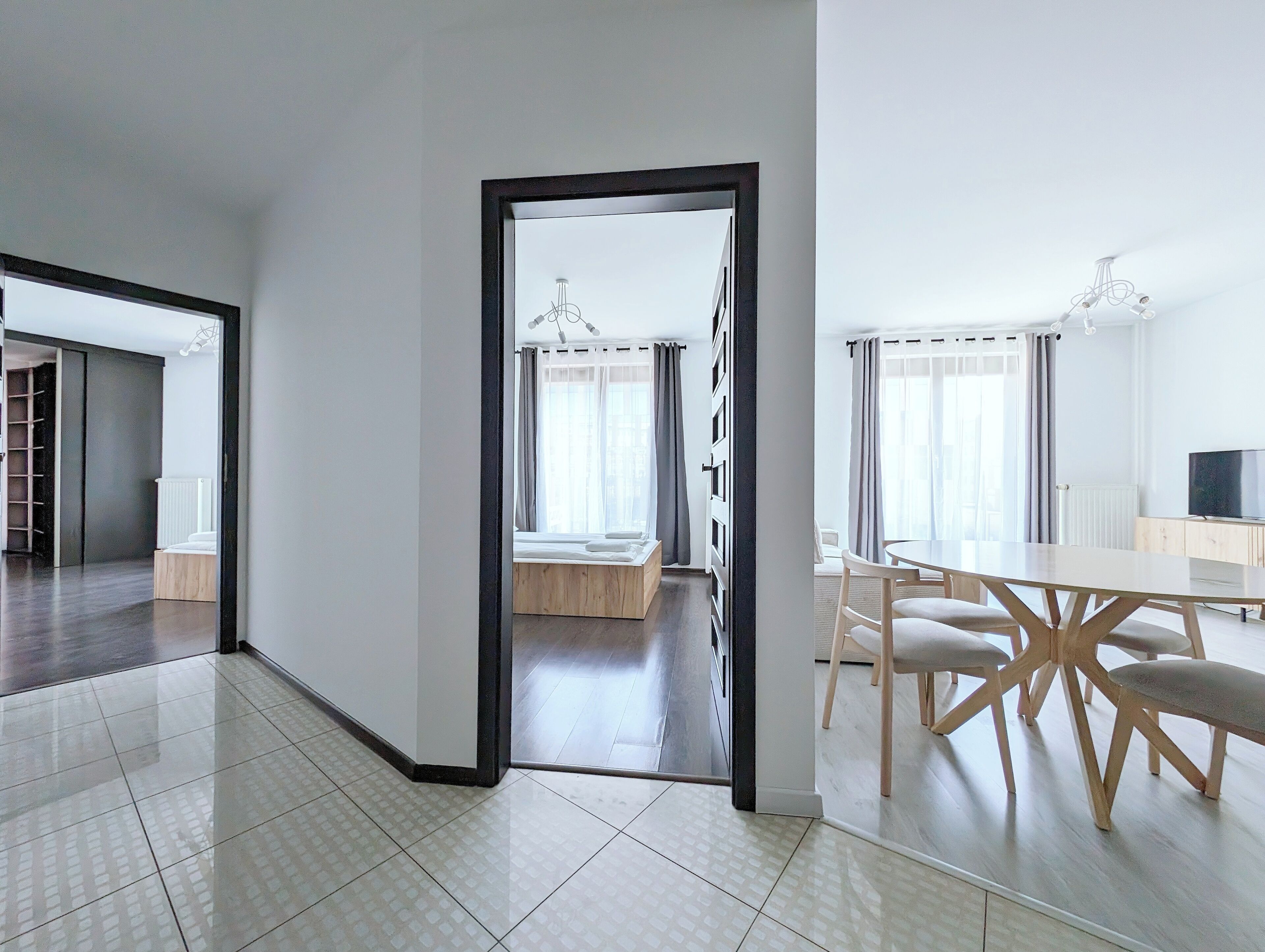 A modern, well-lit room with a dining area, a visible bed, and a hallway leading to another room.