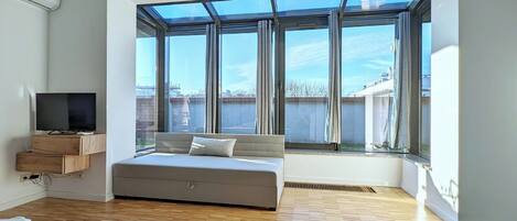 A modern living room with a large window, a sofa, a TV, and a wooden floor.