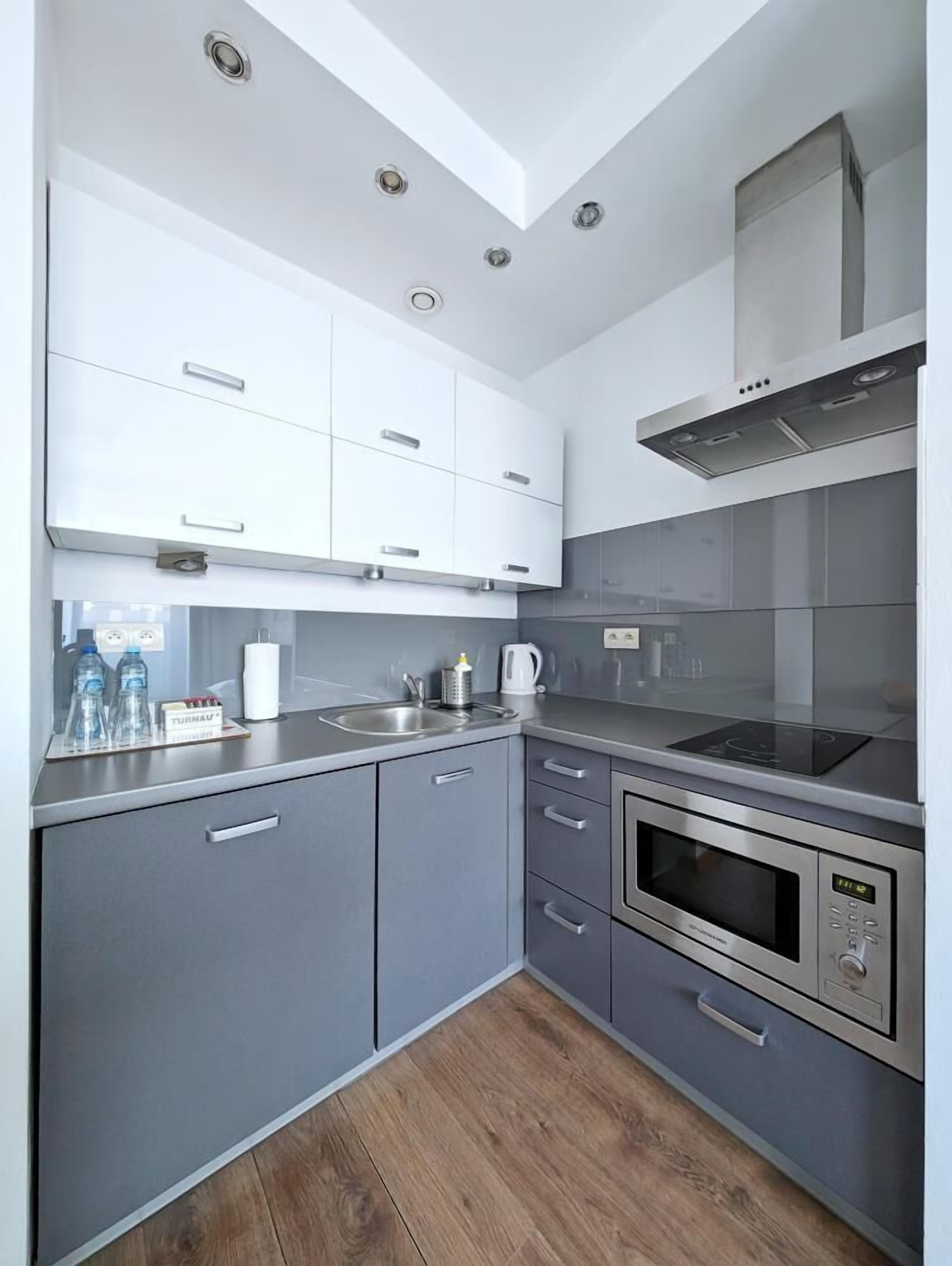 A modern kitchen with grey cabinets, stainless steel appliances, and a wooden floor.