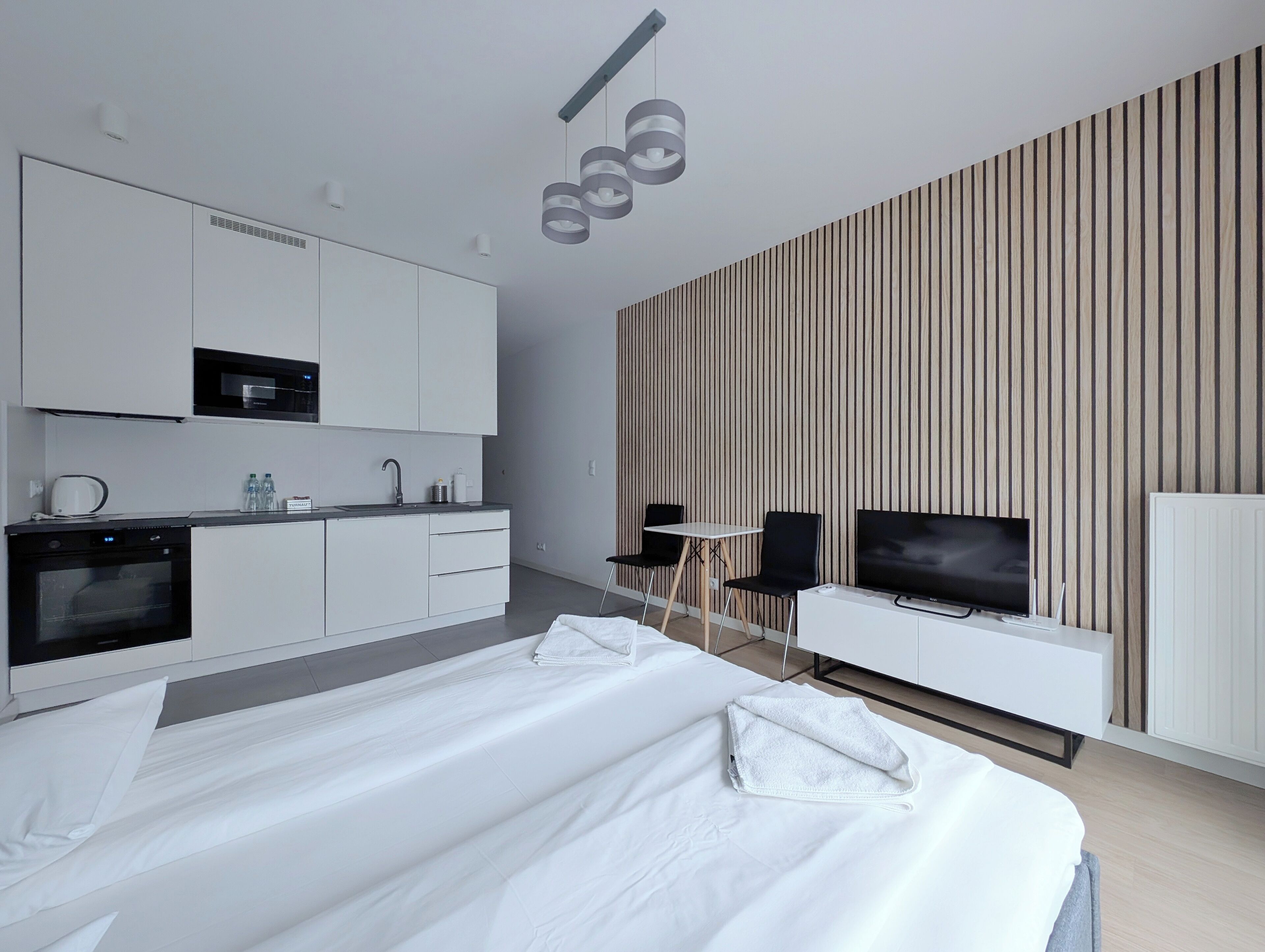 A modern hotel room with a large bed, a kitchenette, a TV, and a striped wall.