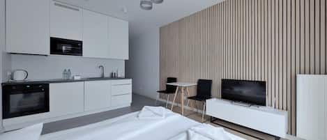A modern hotel room with a large bed, a kitchenette, a TV, and a striped wall.