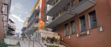 A multi-story residential building with a central staircase, outdoor plants, and a clear sky.