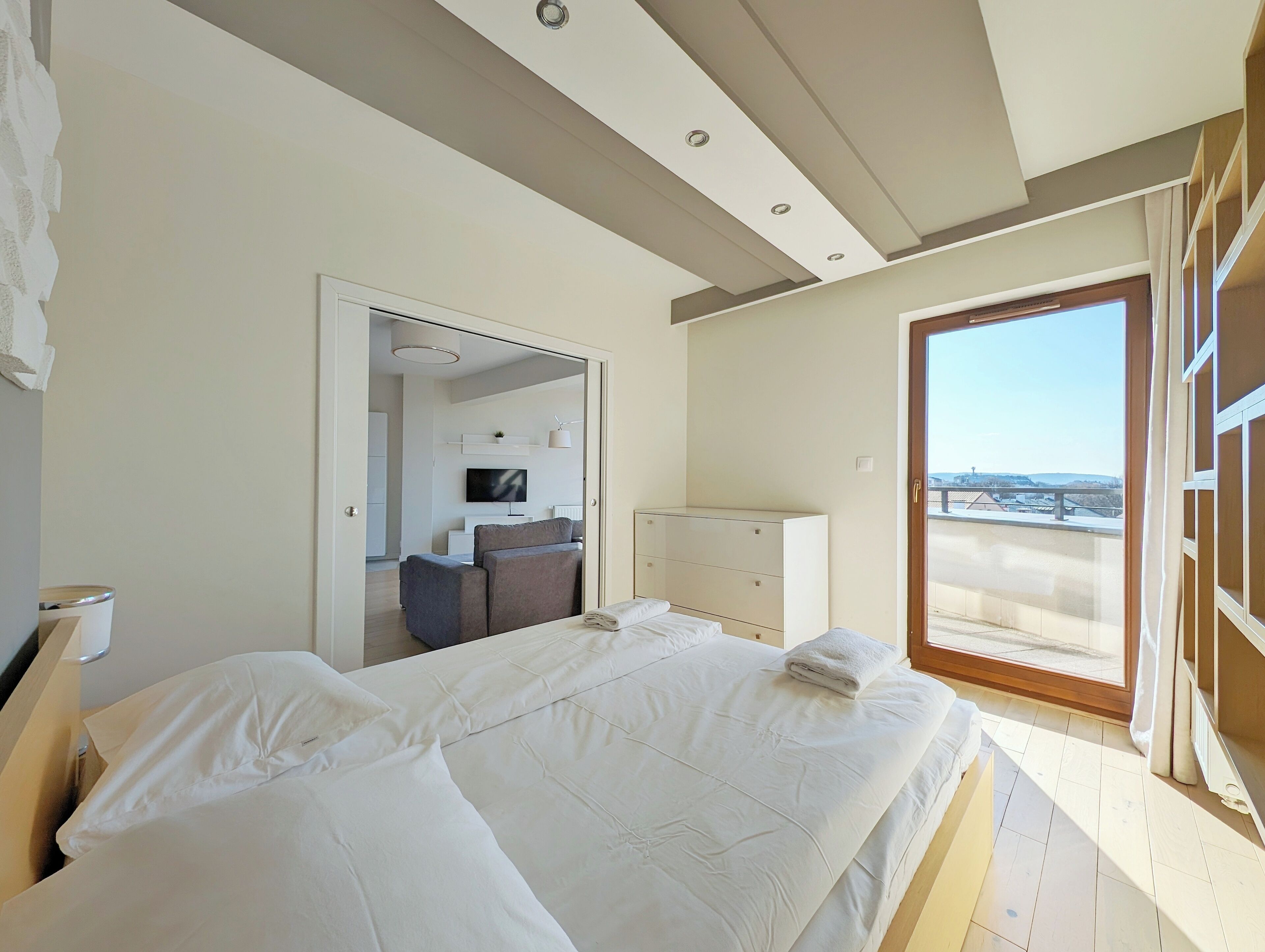 Ein modernes Schlafzimmer mit einem großen Bett, einem Fernseher im Hintergrund und einem Balkon mit Blick.