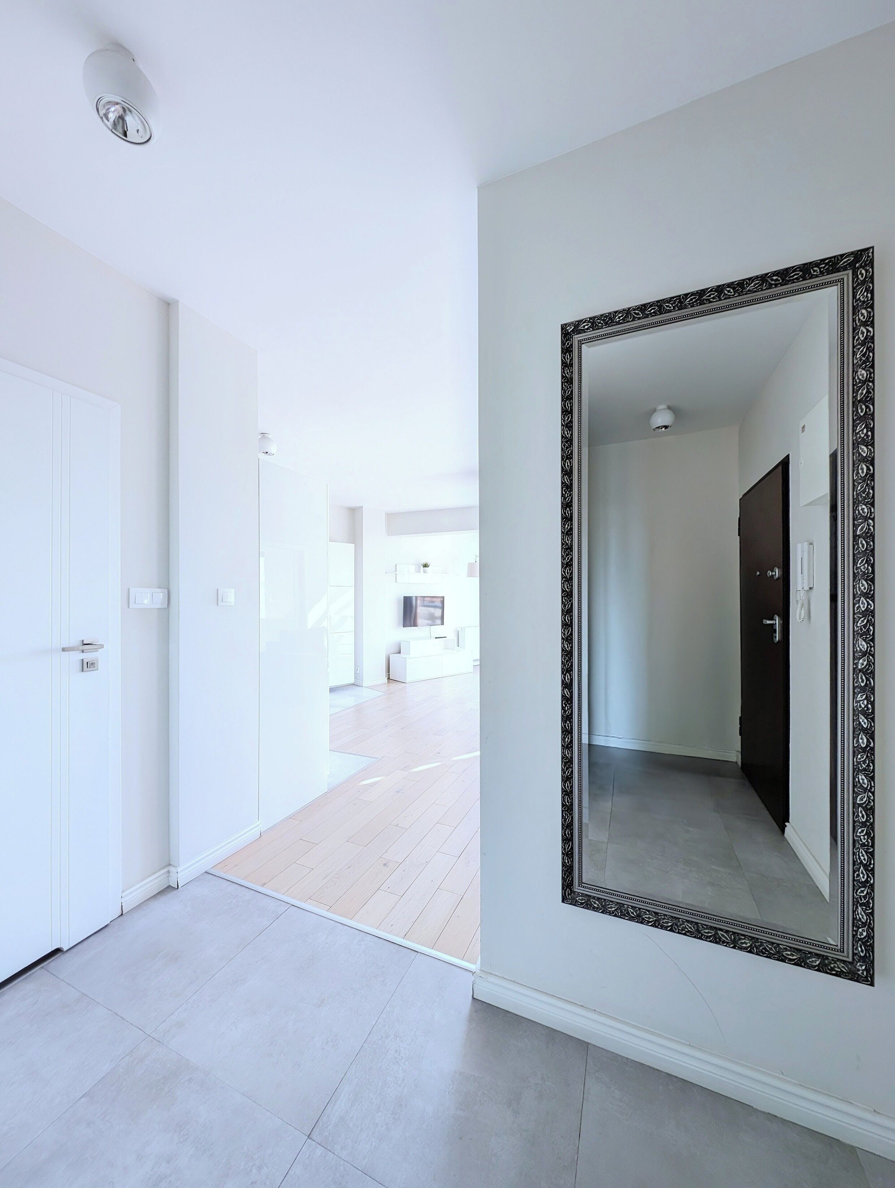 Un couloir avec un grand miroir, des murs blancs et un plancher en bois.