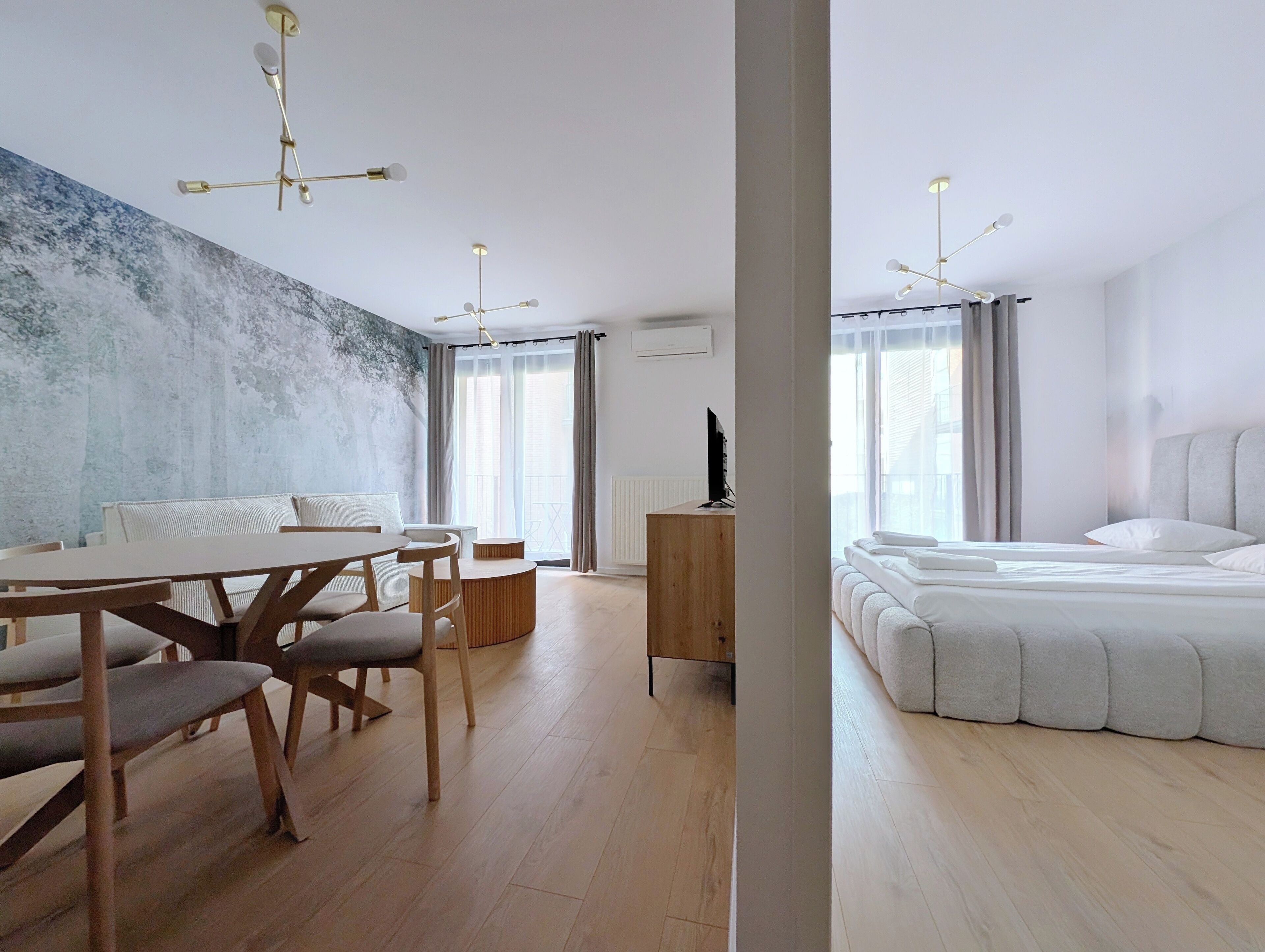 A modern hotel room with a wooden dining table, chairs, a large bed, and a view of the city through the window.