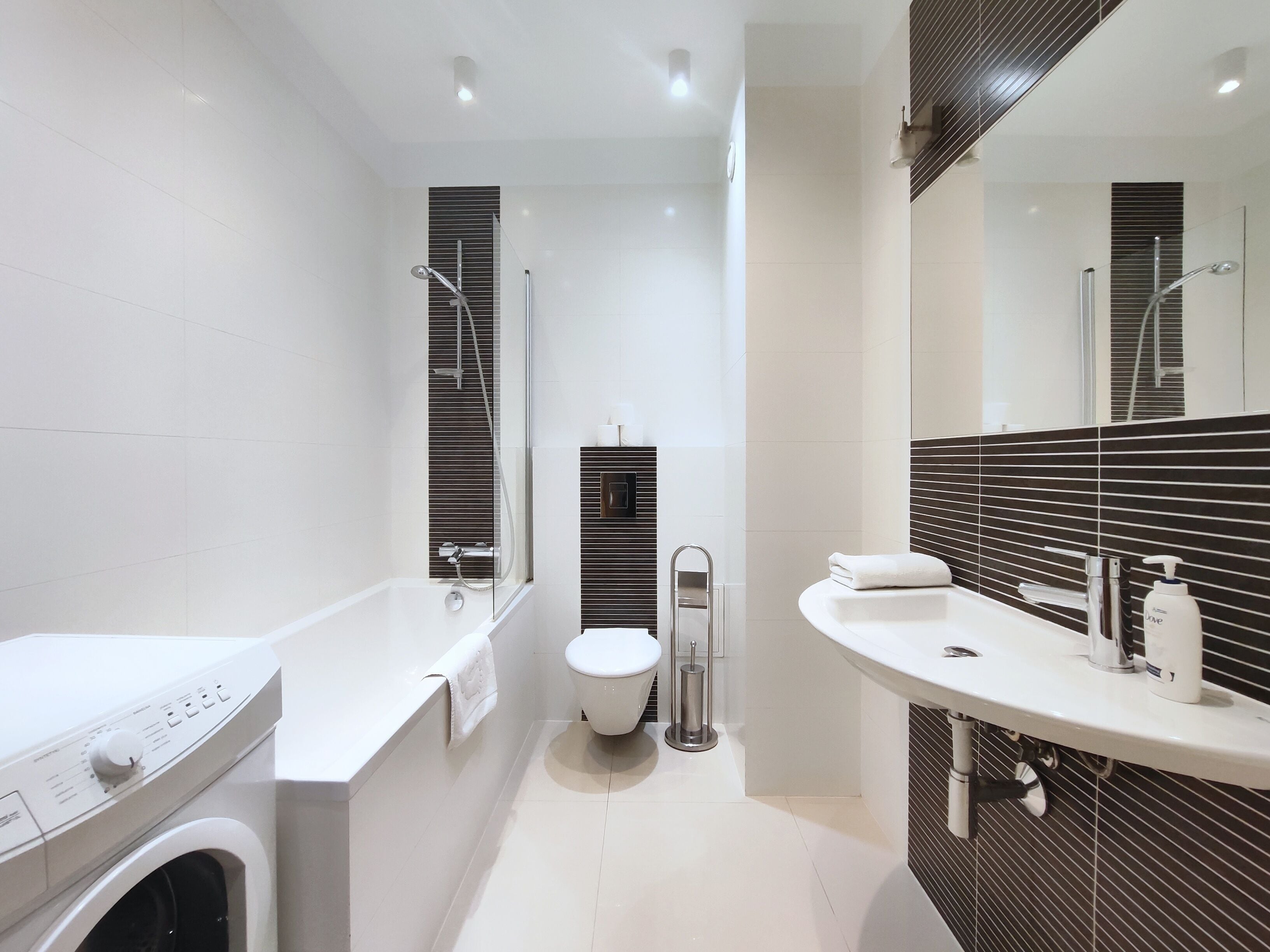 Ein modernes Badezimmer mit Waschmaschine, Toilette und einem großen Spiegel.