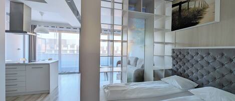 A modern hotel room with a large bed, a dining area, and a view of the city.