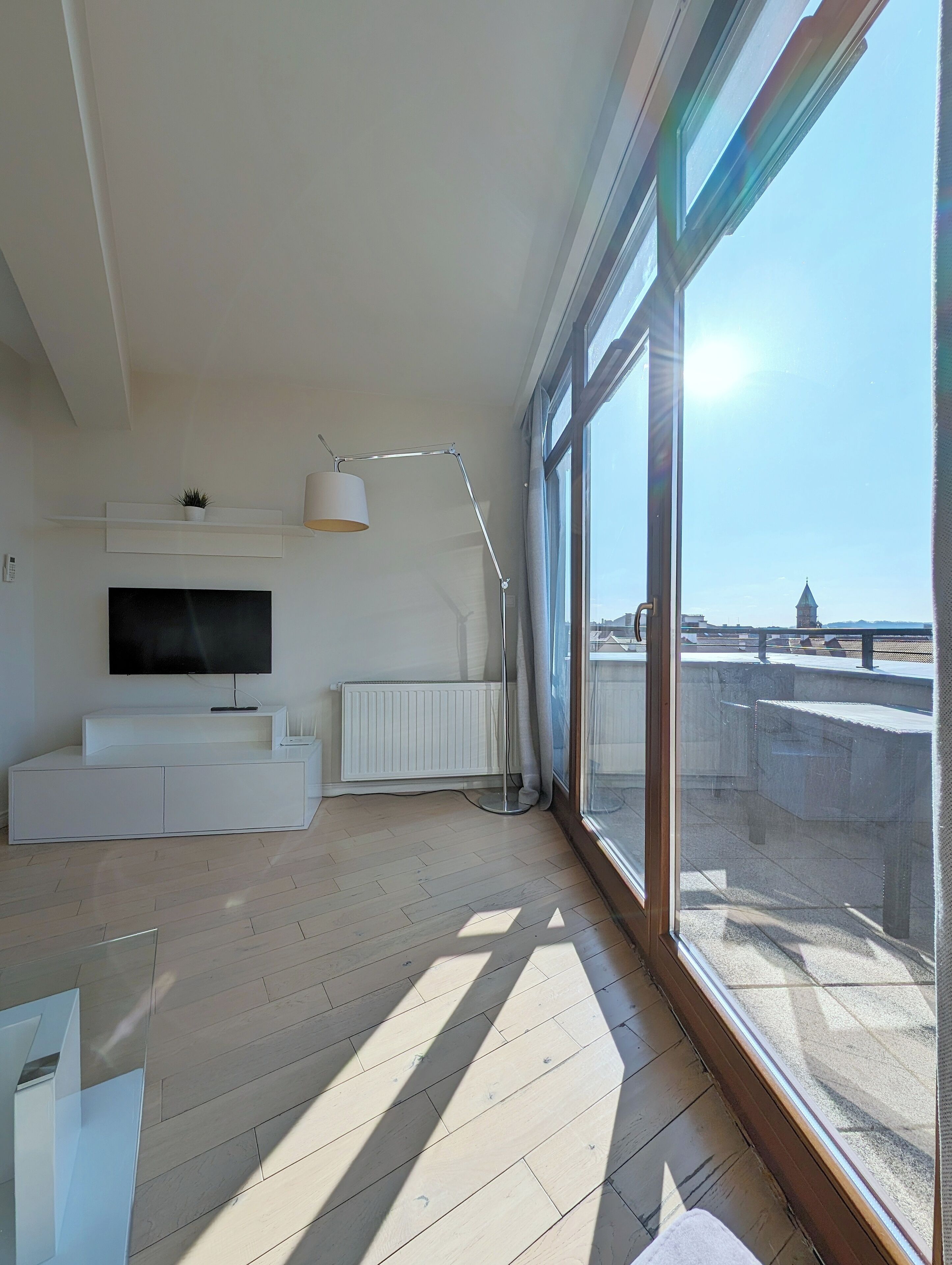 Una sala de estar moderna con un televisor de pantalla plana, un mueble blanco para equipo audiovisual y una lámpara de pie.