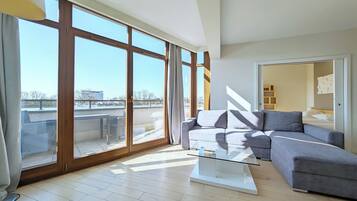 A spacious living room with a large sliding glass door leading to a balcony, a grey sofa, a glass coffee table, and a modern interior design.