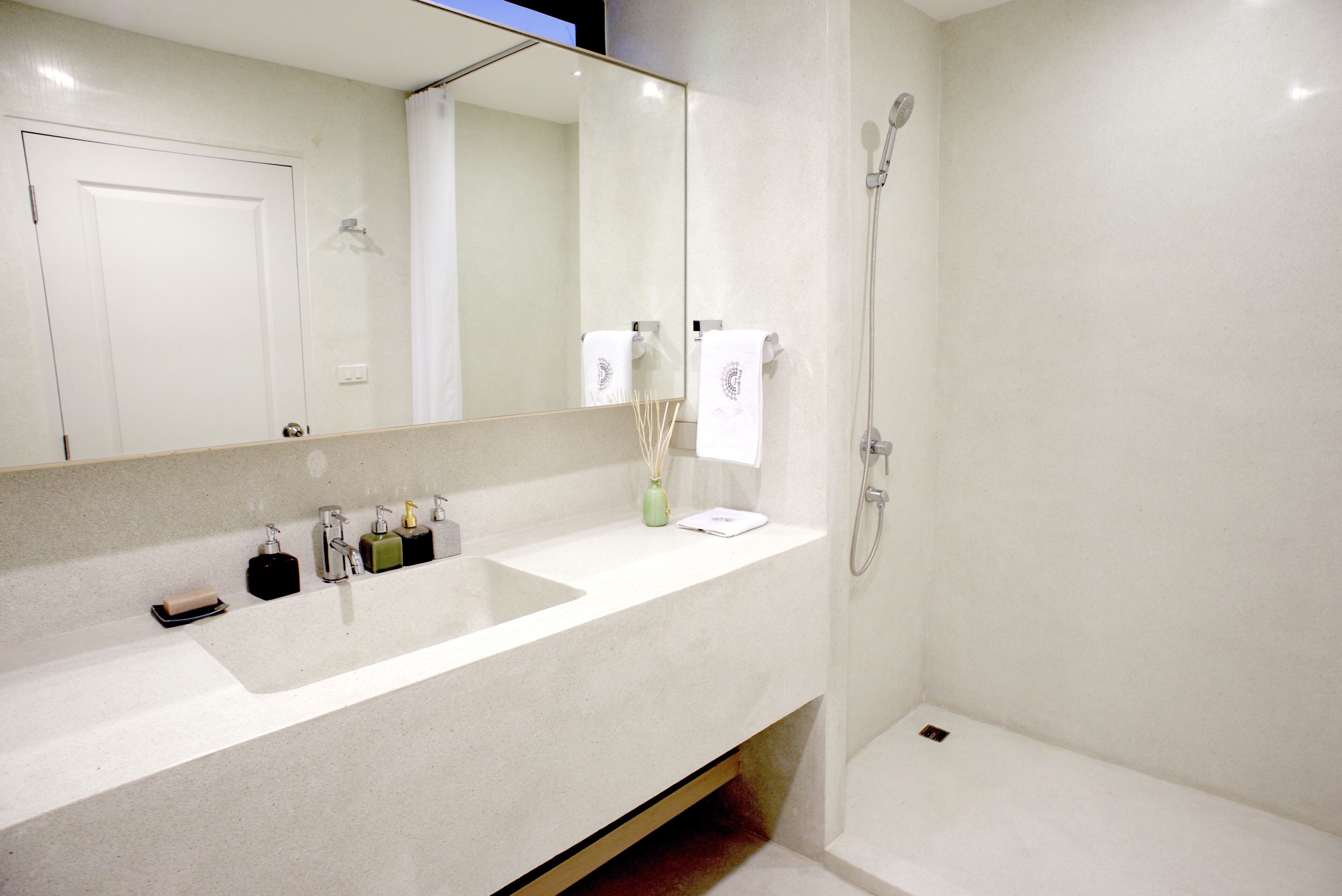 Une salle de bain dotée d’un grand miroir, d’un lavabo avec plusieurs distributeurs de savon, d’un porte-serviettes et d’un espace douche.