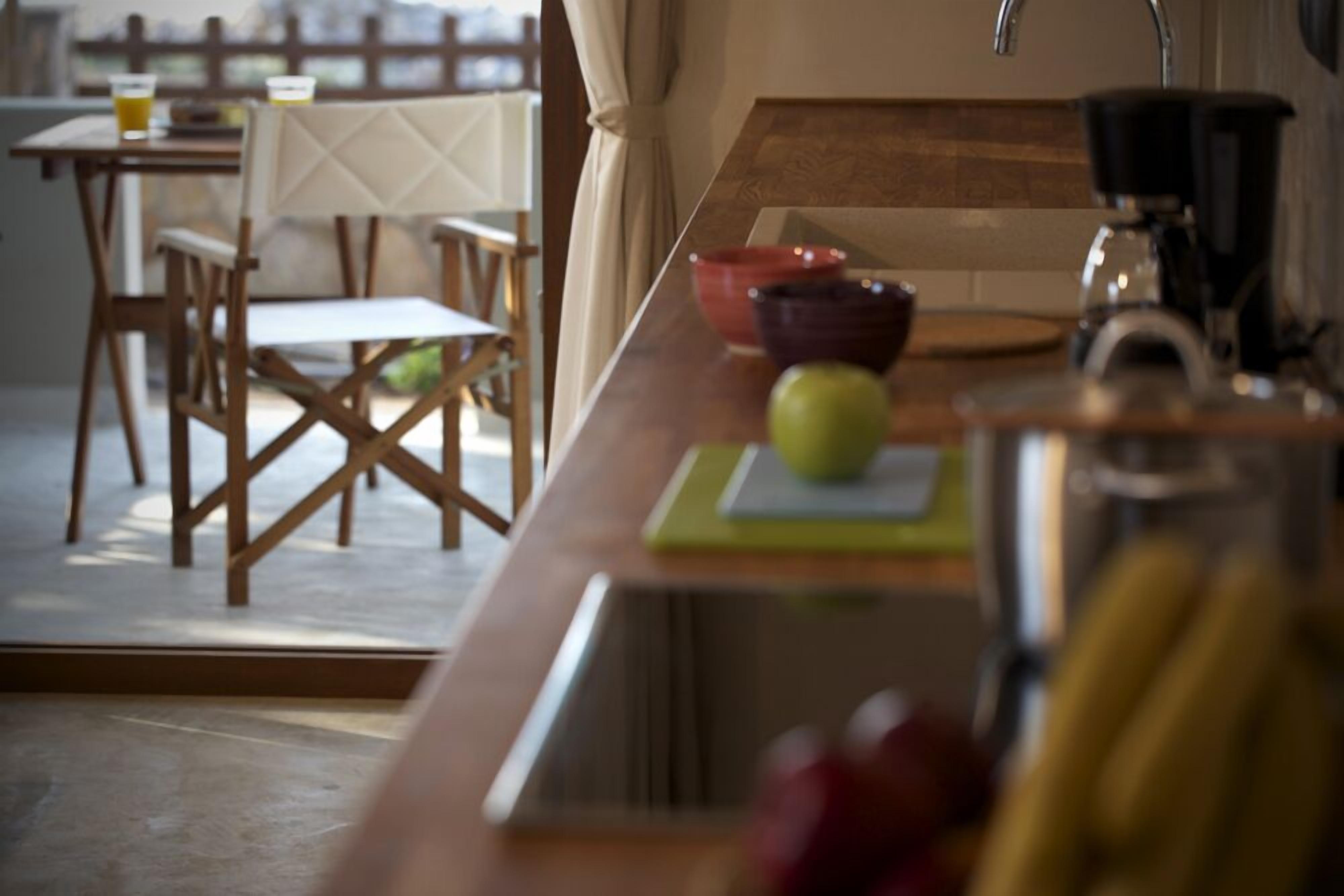 A kitchen with a wooden countertop, a sink, and a coffee maker. There are chairs and a table in the background.