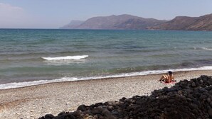 Uma praia com pedras em primeiro plano e montanhas ao fundo.