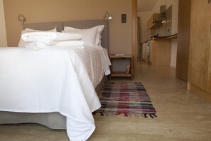 A neatly made bed with folded towels, a bedside table with a book, and a colorful rug on a tiled floor.