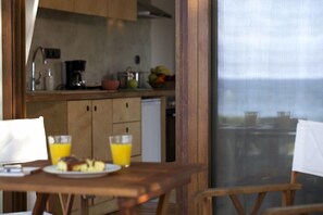 A breakfast table with a plate of food and two glasses of orange juice, a wooden chair, and a view of a kitchen area with cabinets and a coffee maker.
