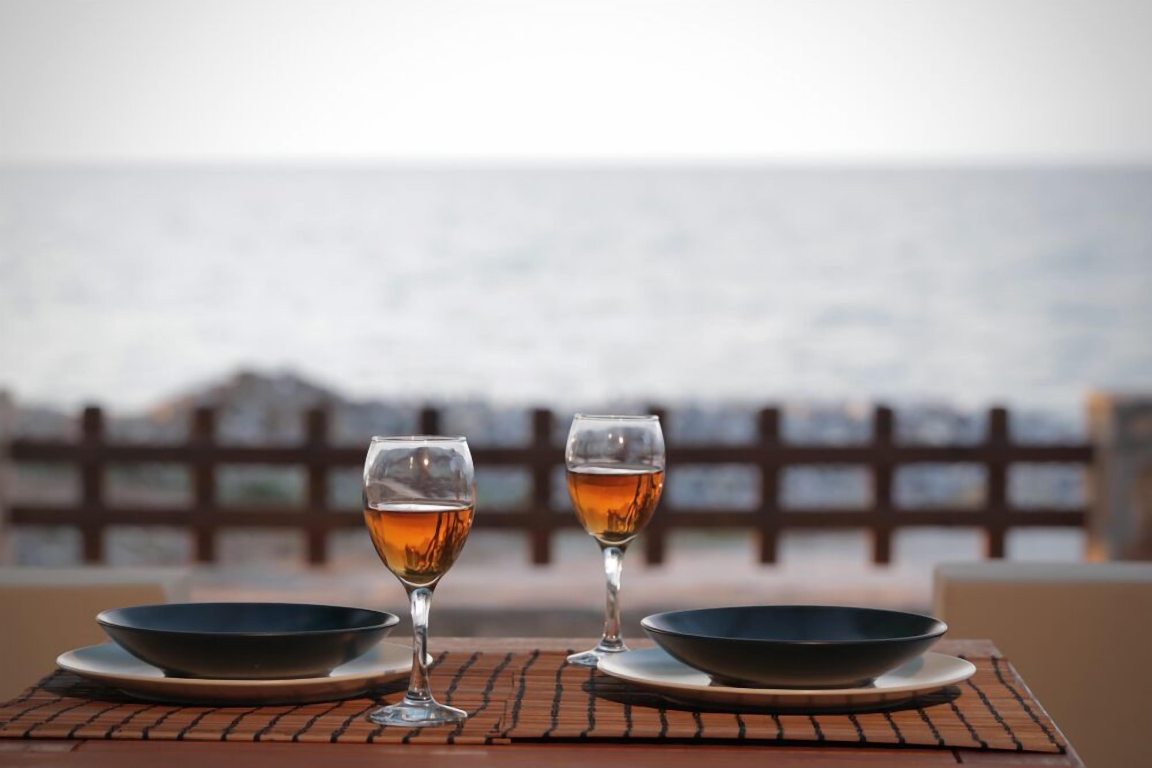 A table with two glasses of amber liquid and two bowls, set against a view of the sea.