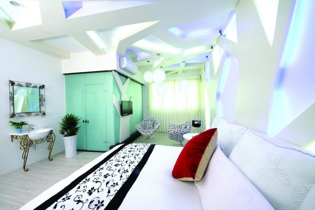 Un dormitorio moderno con una cama, un sofá blanco, un cojín rojo, una puerta verde y una pequeña mesa con una planta.