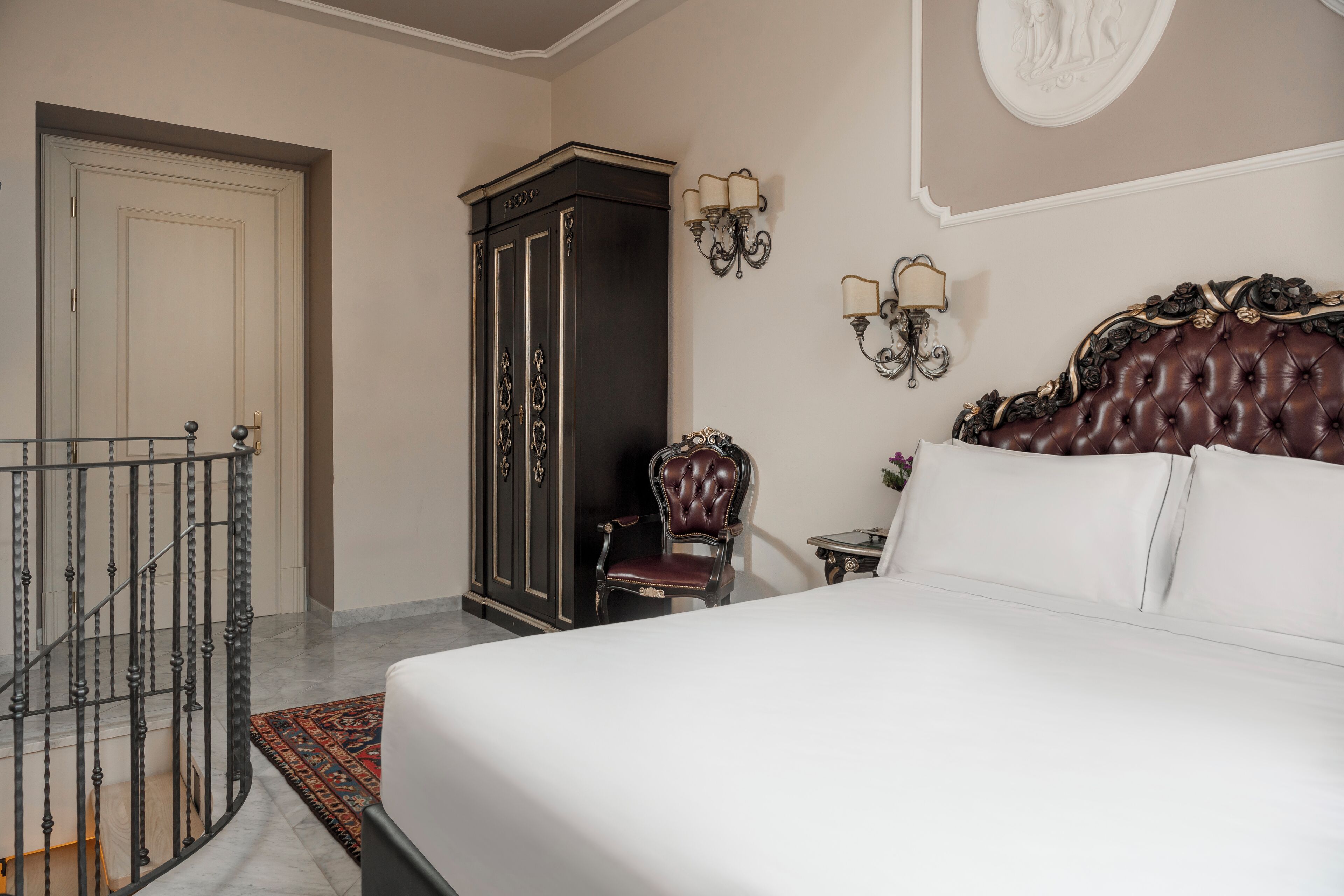 A bedroom with a large bed, a dark wooden wardrobe, a chair, and a small table.