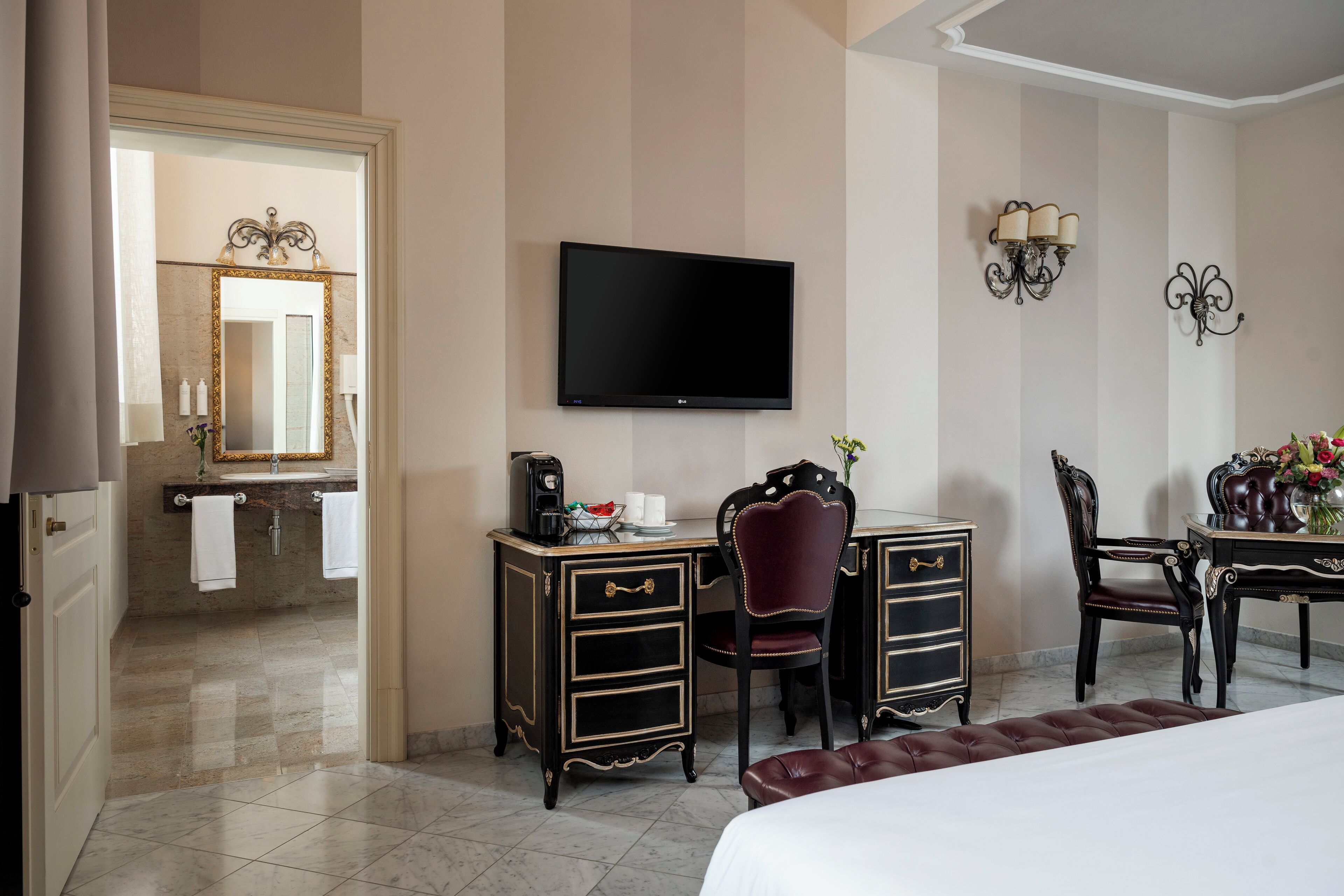 A hotel room with a large bed, a desk with a chair, a television, a mirror, and a bathroom visible through an open door.